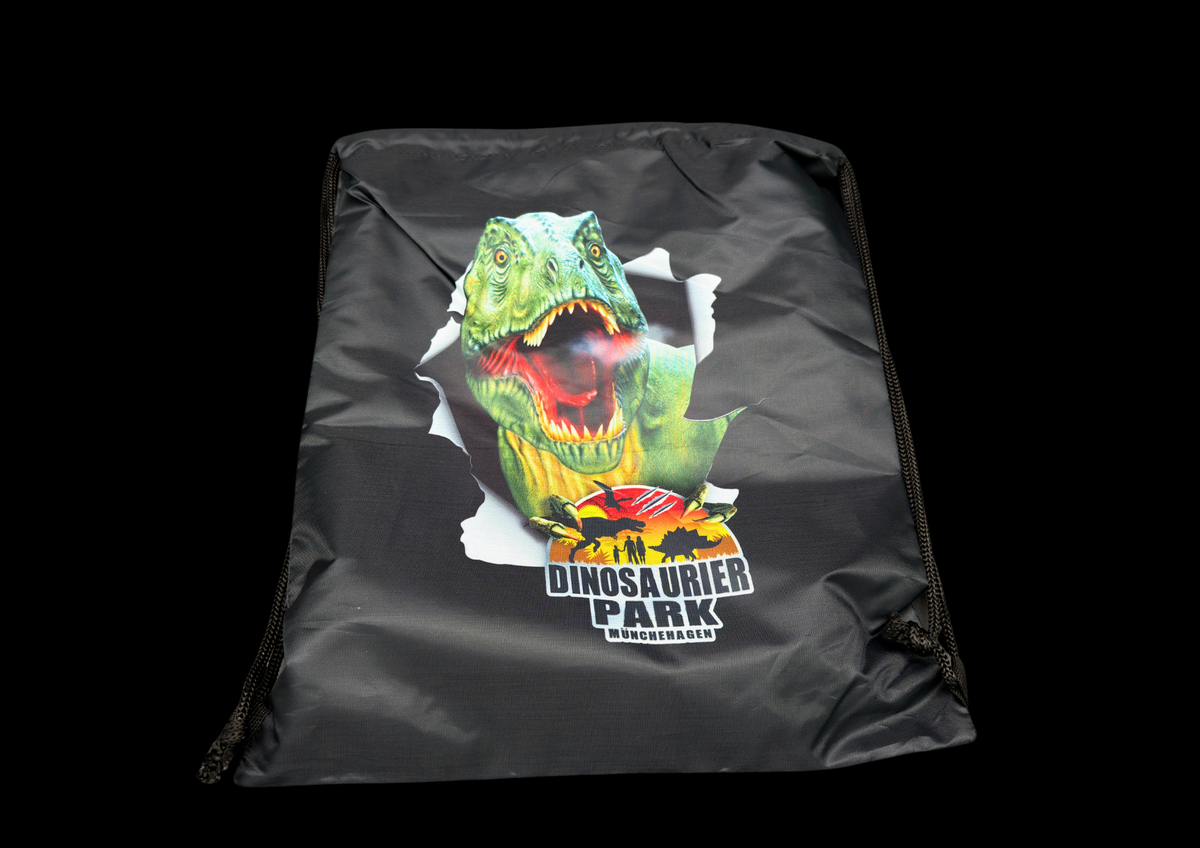 Schwarzer Beutelrucksack mit Dinosaurier-Park Logo im großen Dino Geschenk-Bundle